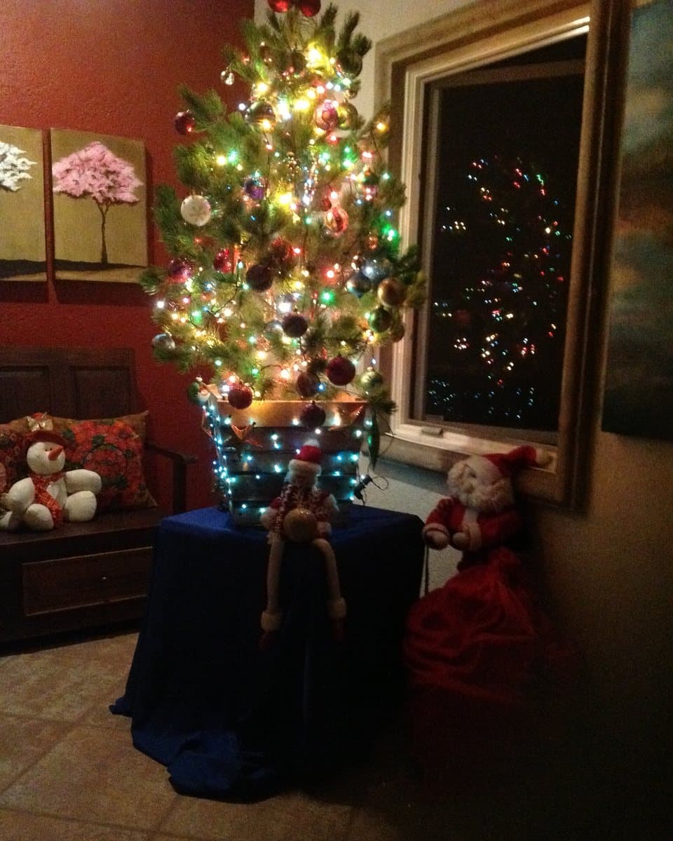 Pino iluminado de noche junto a una ventana, con muñecos navideños